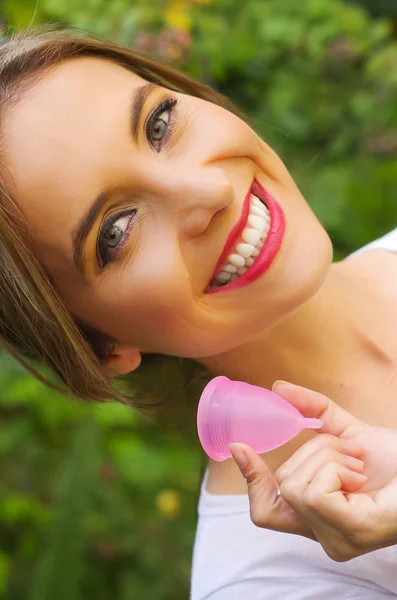Porträt einer jungen lächelnden schönen Frau, die in einer Hand eine Menstruationstasse hält, in einem verschwommenen Hintergrund — Stockfoto