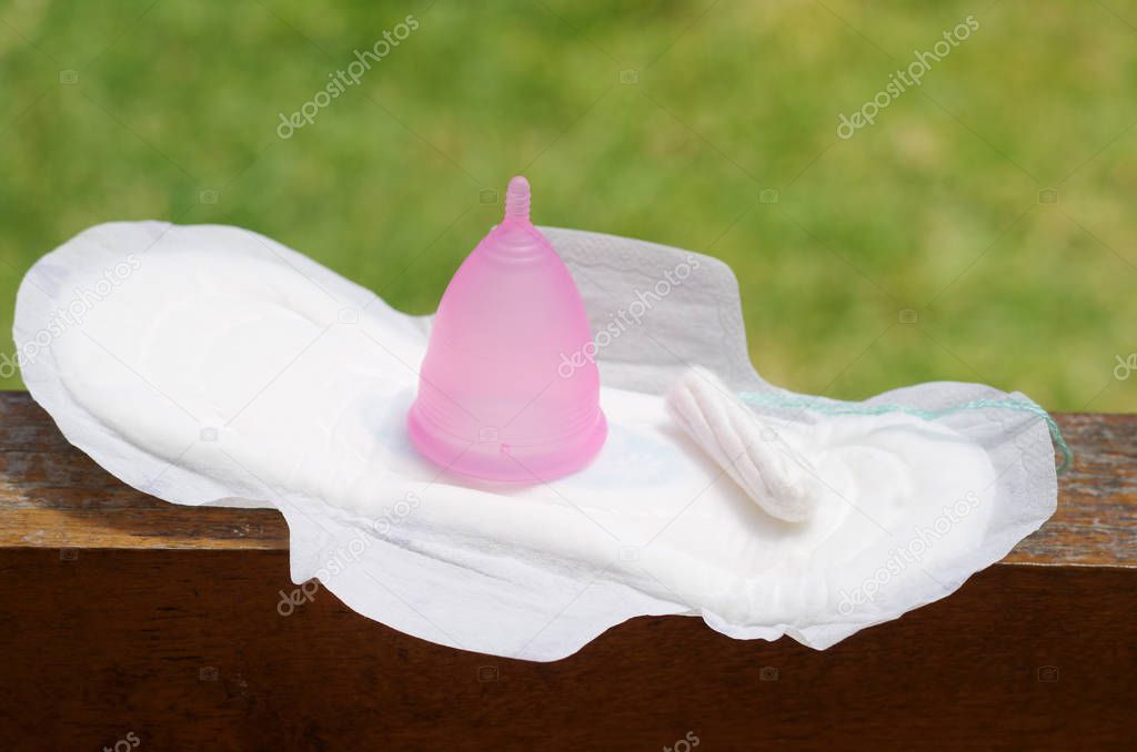 Feminine hygiene product - Menstrual cup over a wooden structure with a tampon of cotton and a hygienic towel, in a blurred background