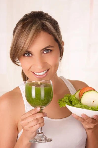 Bela jovem mulher sorridente vestindo uma camiseta branca e segurando uma salada saudável com uma mão e um copo de suco na outra mão — Fotografia de Stock