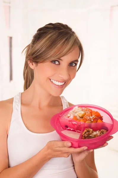 Hermosa joven sonriente mujer usando una camiseta blanca y sosteniendo una ensalada de frutas saludables —  Fotos de Stock