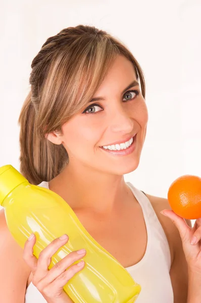 Gros plan d'une belle jeune femme souriante portant un t-shirt blanc et tenant une orange saine et une bouteille d'eau jaune — Photo