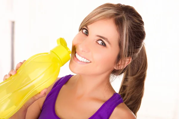 Beautiful smiling woman wearing a purple t-shirt and drinking a yellow bottle of water — Stock Photo, Image