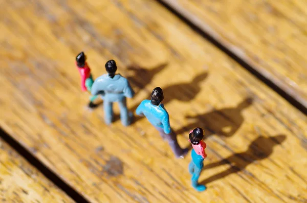 Gente pequeña en miniatura, amiga al aire libre con sombra en el suelo, en un fondo de madera —  Fotos de Stock