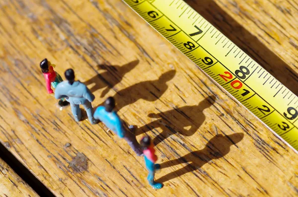 Pequeñas personas en miniatura al aire libre con sombra en el suelo, frente a una cinta métrica en un fondo de madera —  Fotos de Stock