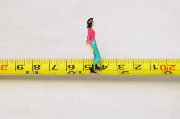 Pequenas pessoas em miniatura mulher andando sobre uma fita métrica amarela isolada — Fotografia de Stock