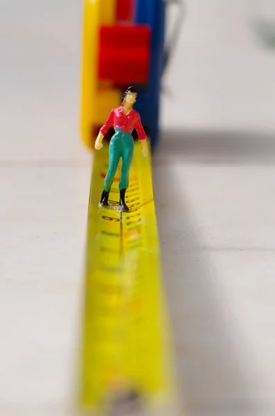 Miniatura gente pequeña mujer caminando sobre una cinta amarilla medida aislado —  Fotos de Stock