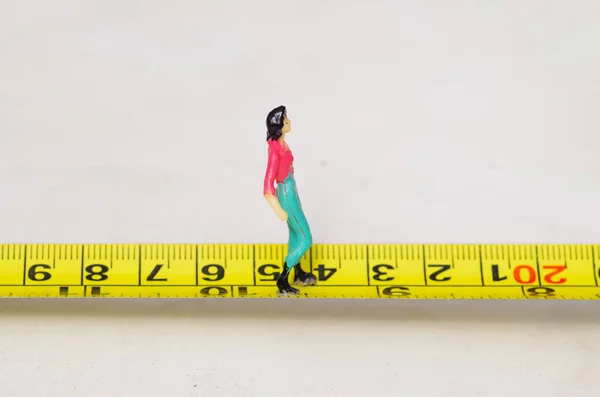Miniature little people woman walking over a yellow tape measure isolated — Stock Photo, Image
