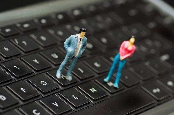 Pequenas pessoas miniatura casal sobre um teclado de computador, em um fundo embaçado — Fotografia de Stock