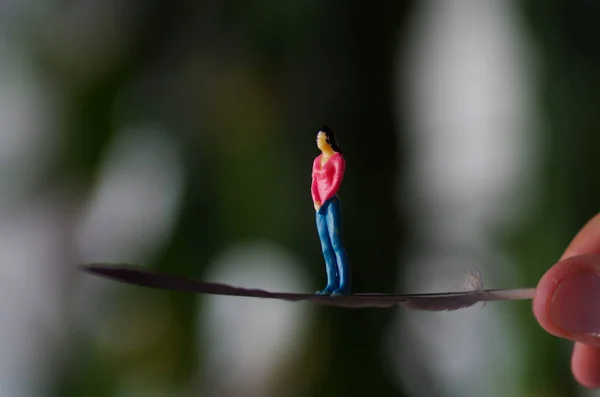 Miniatyr småfolket, kvinna poserar över en fjäder medan en hand håller det, i en suddig bakgrund — Stockfoto