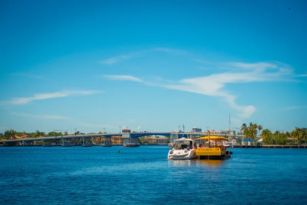 Fort Lauderdale, Amerika Birleşik Devletleri - 11 Temmuz 2017: Renkli sarı su taksi ve birlikte yelken, nehir yürüyüş mesire Fort Lauderdale, Florida'daki arkasında, binaları ile muhteşem bir manzarasına sahip bir beyaz yat — Stok fotoğraf
