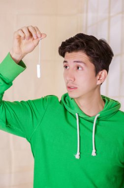 Bulanık bir arka planda yeşil kapüşonlu bir adet pamuk tampon tutan bir sürpriz yüz yakışıklı adamla