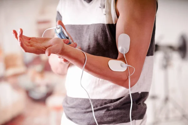 Close-up of a man holding an electrode machine in his hand and with electrostimulator electrodes in the arm of a fitness young man in a blurred background — Stock Photo, Image