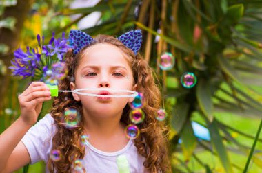 Mavi kulakları kaplan Aksesuar bulanık doğa arka planda onun Merkez over sabun köpüğü bir yaz niteliğine oynamaktan mutlu küçük kıvırcık kız giyiyor