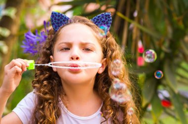 Mavi kulakları kaplan Aksesuar bulanık doğa arka planda onun Merkez over sabun köpüğü bir yaz niteliğine oynamaktan mutlu küçük kıvırcık kız giyiyor