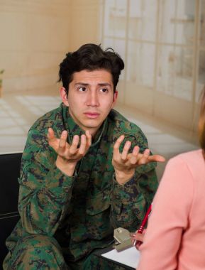 Burred arka planda bir tıbbi sağlık merkezinde terapist konuşmak savaştan sonra travma sonrası stres bozukluğu acı yakışıklı mutsuz genç asker giyen üniforma