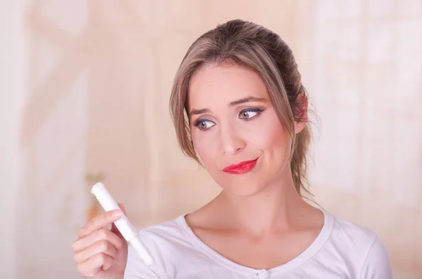 Young beautiful woman with a worried face, holding a menstruation cotton tampon in her hand, in a blurred background — Stock Photo, Image