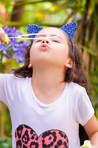 Happy little girl playing with soap bubbles on a summer nature, wearing a blue ears tiger accessories over her head in a blurred nature background — Stock Photo, Image