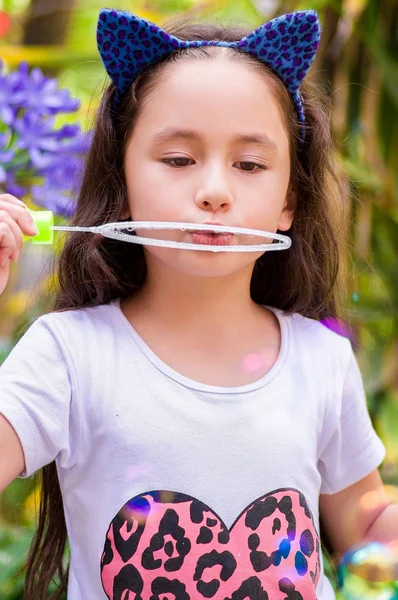 Happy little girl playing with soap bubbles on a summer nature, wearing a blue ears tiger accessories over her head in a blurred nature background — Stock Photo, Image