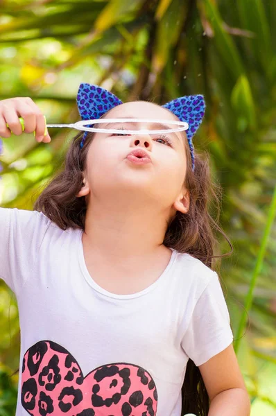 Feliz niña jugando con burbujas de jabón en una naturaleza de verano, con un tigre orejas azules accesorios sobre su cabeza en un fondo de naturaleza borrosa —  Fotos de Stock