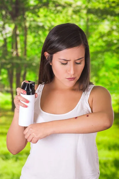 Close up of young woman suffering from itch after mosquito bites, using a spay over the insect bite, allergic skin treatment concept, in a green forest background — Stock Photo, Image