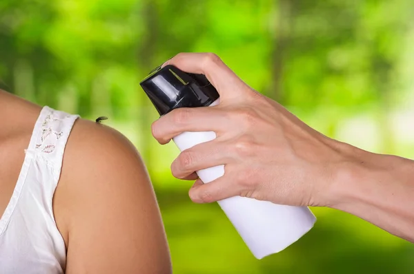 Gros plan d'une jeune femme avec un moustique à l'épaule pendant qu'une main d'homme utilise un vaporisateur sur l'insecte pour le tuer, dans un fond flou — Photo