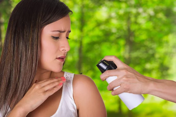 Close up of beautiful young woman looking at her shoulder while a man hand is using a spay over the insect to kill it, in a blurred background — Stock Photo, Image