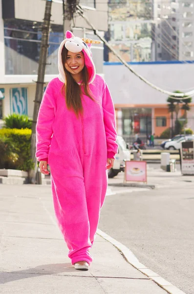 Закройте глаза на красивую улыбчивую молодую женщину в розовом костюме единорога, идущую по улицам города Кито — стоковое фото