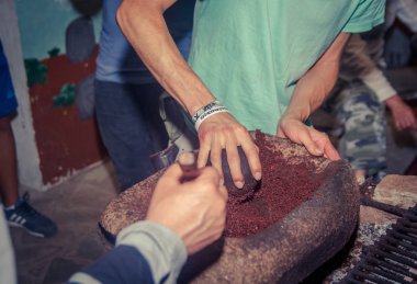 İnsanlar bir odun sobası yanındaki bir taş üzerine kakao çekirdekleri taşlama