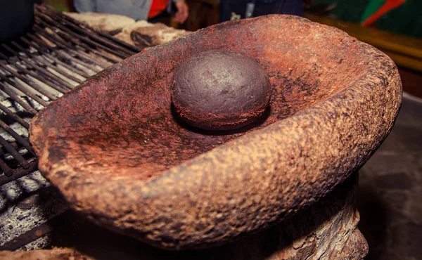 Закрыть древний раствор, чтобы измельчить какао-бобы над скалой, рядом с дровяной печью — стоковое фото