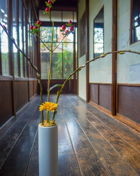 Close up of a flower vase with a yellow flower and red branch at indoor view of hall with a wooden floor, in Kyoto, Japan — Stock Photo, Image