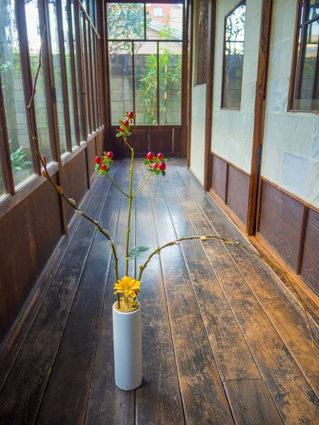 Close up of a flower vase with a yellow flower and red branch at indoor view of hall with a wooden floor, in Kyoto, Japan — Stock Photo, Image