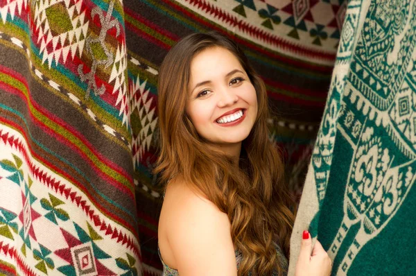 Gros plan d'une belle jeune femme souriante touchant les vêtements traditionnels andins et posant pour caméra, fond de tissus colorés — Photo
