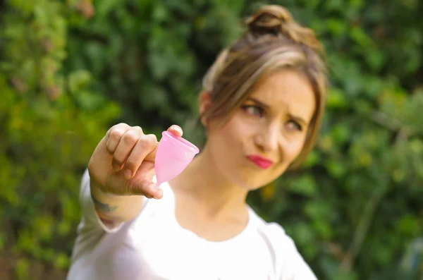 Primer plano de una joven mujer señalando delante de ella una copa menstrual en una mano, concepto de ginecología, en un fondo borroso — Foto de Stock