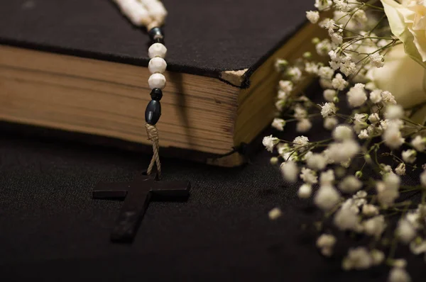 Kutsal İncil ile bulanık beyaz küçük çiçekler, siyah arka plan üzerinde bir tespih yakın çekim