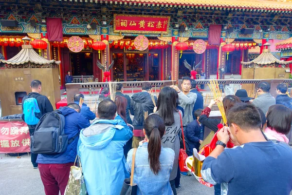 HONG KONG, CHINA - 22 DE ENERO DE 2017: Multitud de personas sosteniendo sus manos con palos de incienso y rezando dentro del templo budista Wong Tai Sin para orar, en Hong Kong, China — Foto de Stock