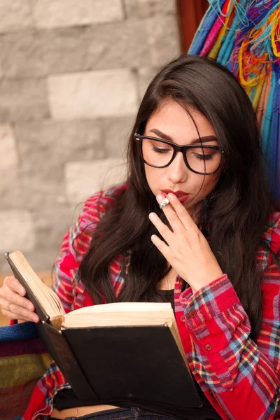 Vackra unga hipster kvinnan avslappnande och liggande i en färgglad hängmatta, readinga bok och rökning njuter sitt liv — Stockfoto