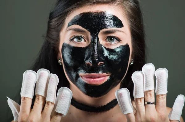 Närbild av en skönhet ung kvinna med en svart ansiktsmask och bär naglar protector i hennes naglar, i en svart bakgrund — Stockfoto