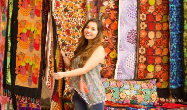 Güzel gülümseyen genç kadın and dokunmadan geleneksel Giyim Tekstil iplik ve dokuma tarafından el yün, renkli kumaşlar arka planda