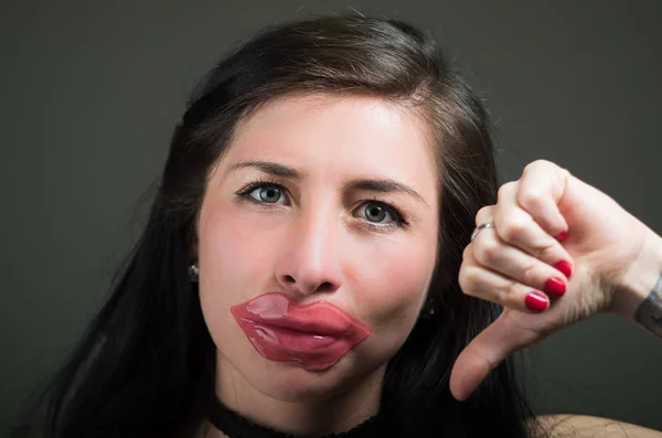 Schöne natürliche Frau mit Lippen rosa Maske mit einem Daumen nach unten, Wellness-Behandlungen. Kosmetologie vor dunklem Hintergrund — Stockfoto