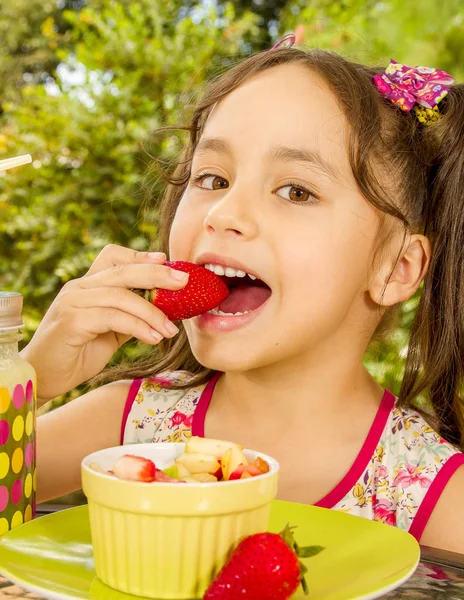 Mooi jong meisje, eten van een gezonde aardbei met haar hand met een fruit salade over een houten tafel, in een tuin achtergrond — Stockfoto
