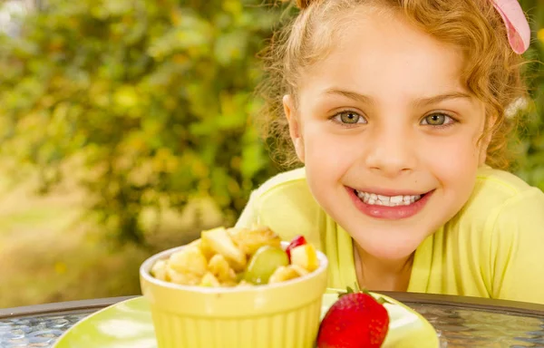 Egy gyönyörű fiatal lány sárga pólóban, arra készül, hogy enni egy egészséges gyümölcsöt, salátát, a kerti háttérben közelről — Stock Fotó
