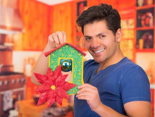 QUITO, ECUADOR - 17 OCTOBER, 2015: Close up of a surprised handsome young man holding in his hand a christmas tree decoration in a blurred background — стоковое фото