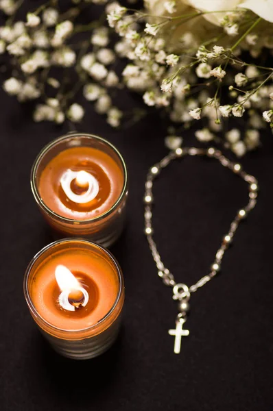 Rosary beads with two blurred orange candles and small flowers, black background, above view — Stock Photo, Image