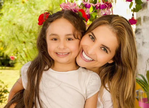 Souriant belle maman étreignant sa jolie fille en robe beige portant deux cravates rouges dans les cheveux — Photo