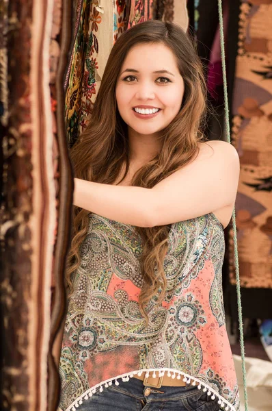 Gros plan de belle jeune femme souriante touchant les vêtements traditionnels andins et posant pour la caméra, fond de tissus colorés — Photo