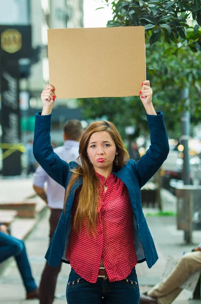 Young woman wearing casual clothes standing outdoors holding up cardboard poster, protesting concept — Stock Photo, Image