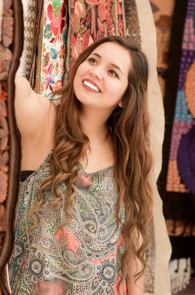 Gros plan de belle jeune femme souriante touchant les vêtements traditionnels andins et posant pour la caméra, fond de tissus colorés — Photo