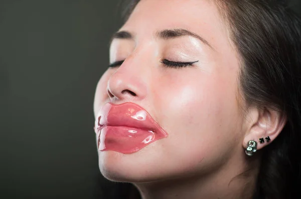 Close up of a beautiful natural girl woman with a lip pink mask, spa treatments. Cosmetology in a dark background — Stock Photo, Image