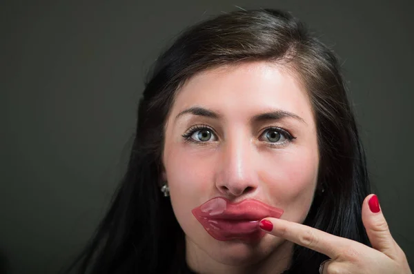 Bella donna ragazza naturale che punta con la mano al viso una maschera rosa labbra, trattamenti termali. Cosmetologia in uno sfondo scuro — Foto Stock
