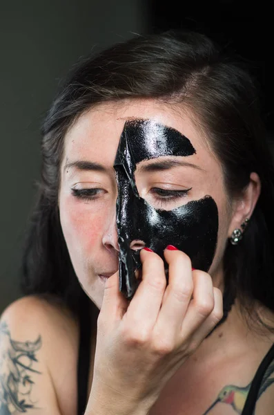 Close up of a beauty young woman taking off a black face mask — Stock Photo, Image